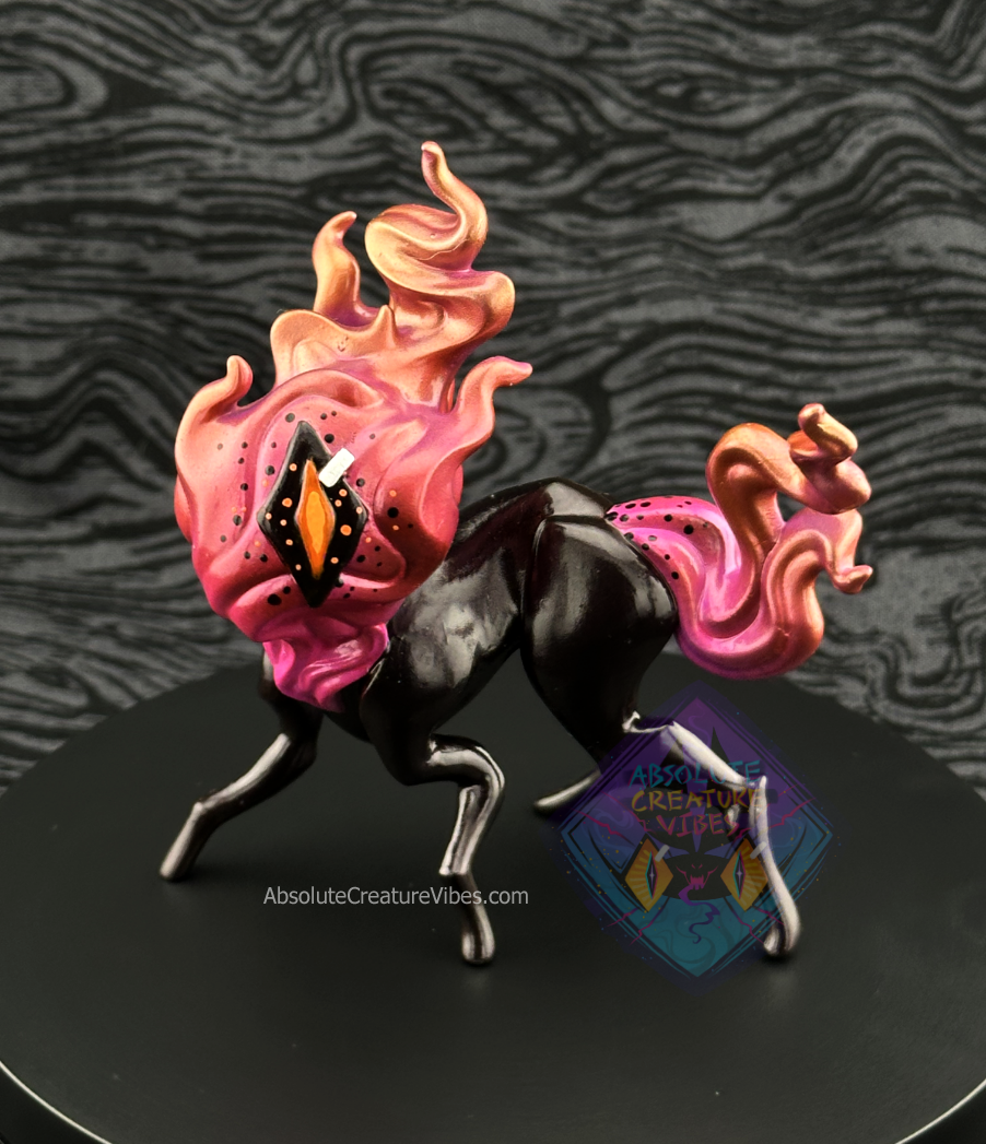 Four legged creature with flaming head and tail, one eye in the center. Pink, Copper, and Gold flame, black body, sclera; orange pupil.