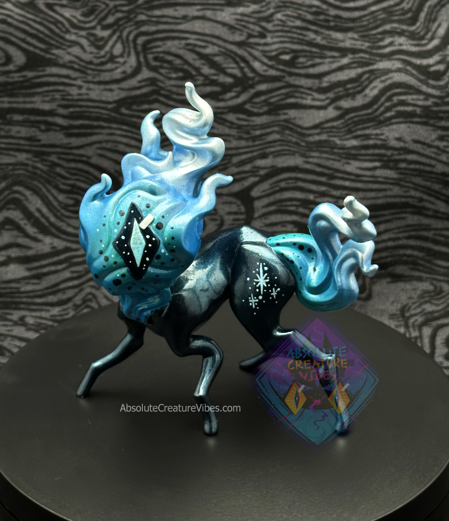Four legged creature with flaming head and tail, one eye in the center. Blue and silver flame, blueish black metallic body, sclera, light blue and silver pupil.