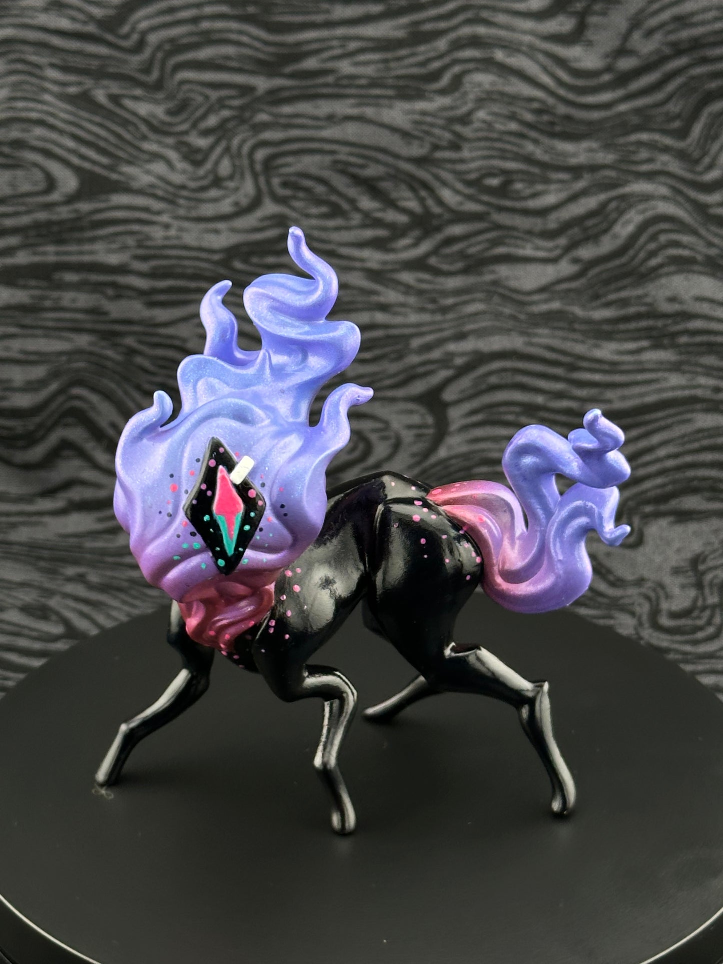 Four legged creature with flaming head and tail, one eye in the center. Pink and purple flame, eye; black body, sclera.