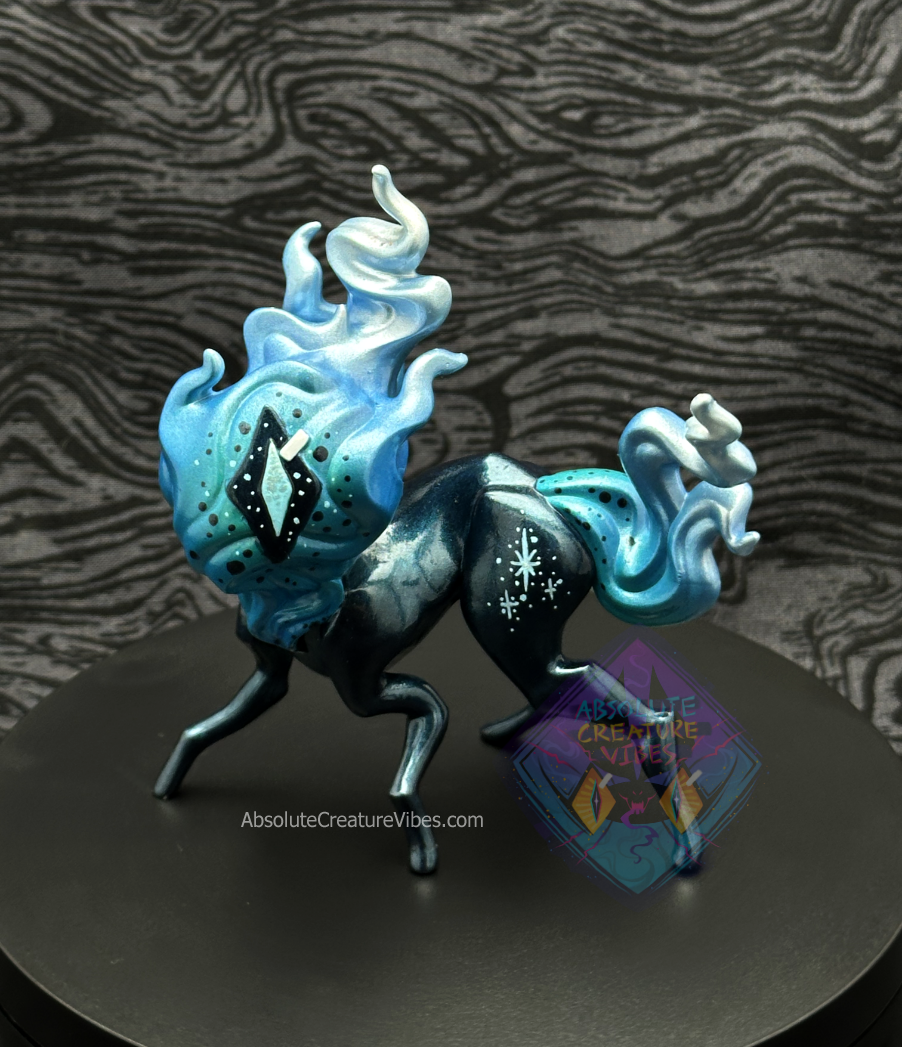 Four legged creature with flaming head and tail, one eye in the center. Blue and silver flame, blueish black metallic body, sclera, light blue and silver pupil. 