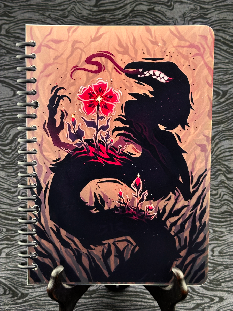 Spiral bound notebook cover featuring black worm with pink flower growing from a wound on a tan background.